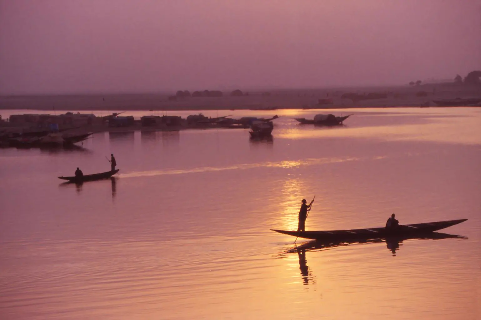 Pirogues et pêcheurs sur le fleuve au coucher du soleil, dans une lumière rose